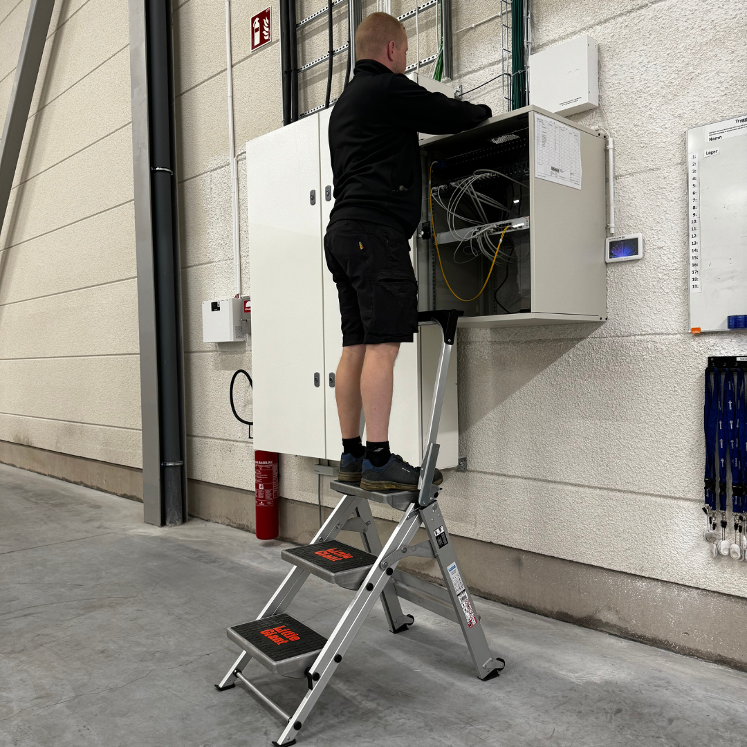 Elektriker står på trappestige Easystep og arbeider i et koblingsskap