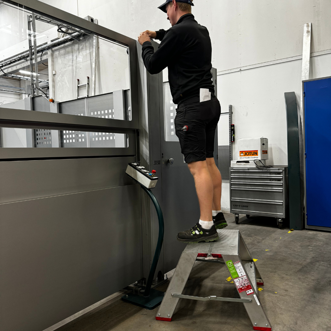 Håndverker står på arbeidsbukk Pro Podium XL og betjener en maskin i industrihall